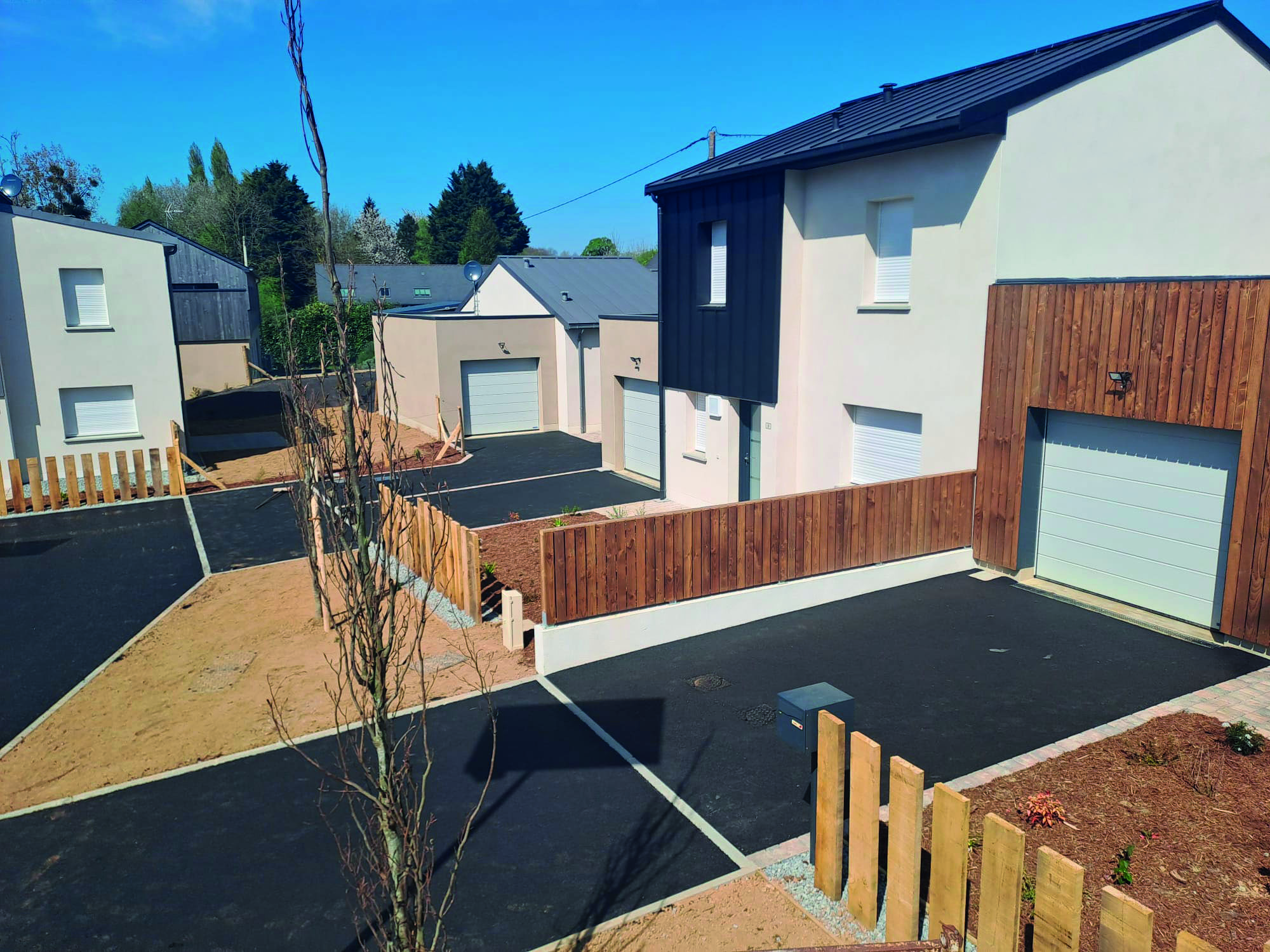 Cour en enrobé devant une maison neuve, bordée d'une clôture en bois