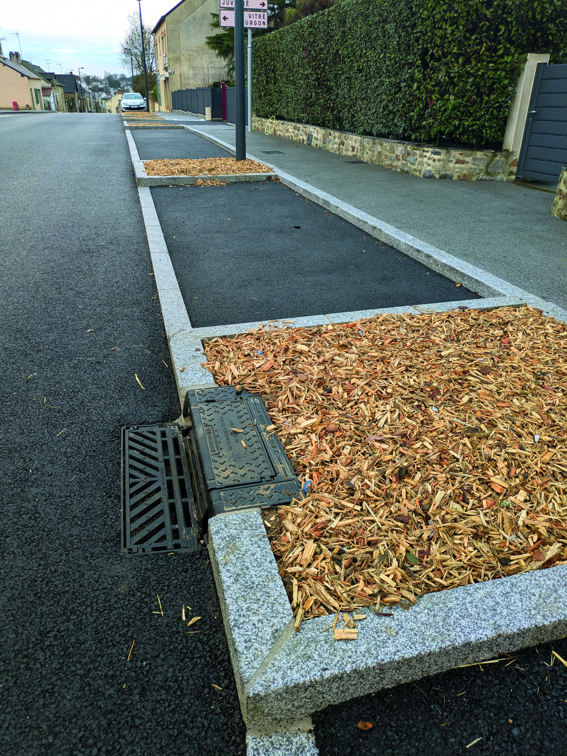 Trottoir en enrobé bordé d'une bande de paillage et de bordures en granit