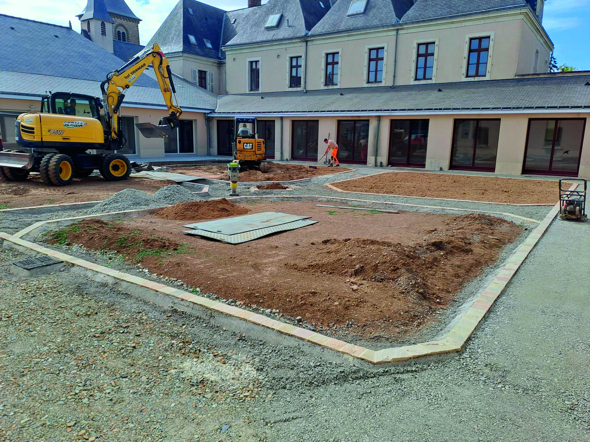 Pelleteuse terrassant une cour devant un bâtiment, bordures déjà posées