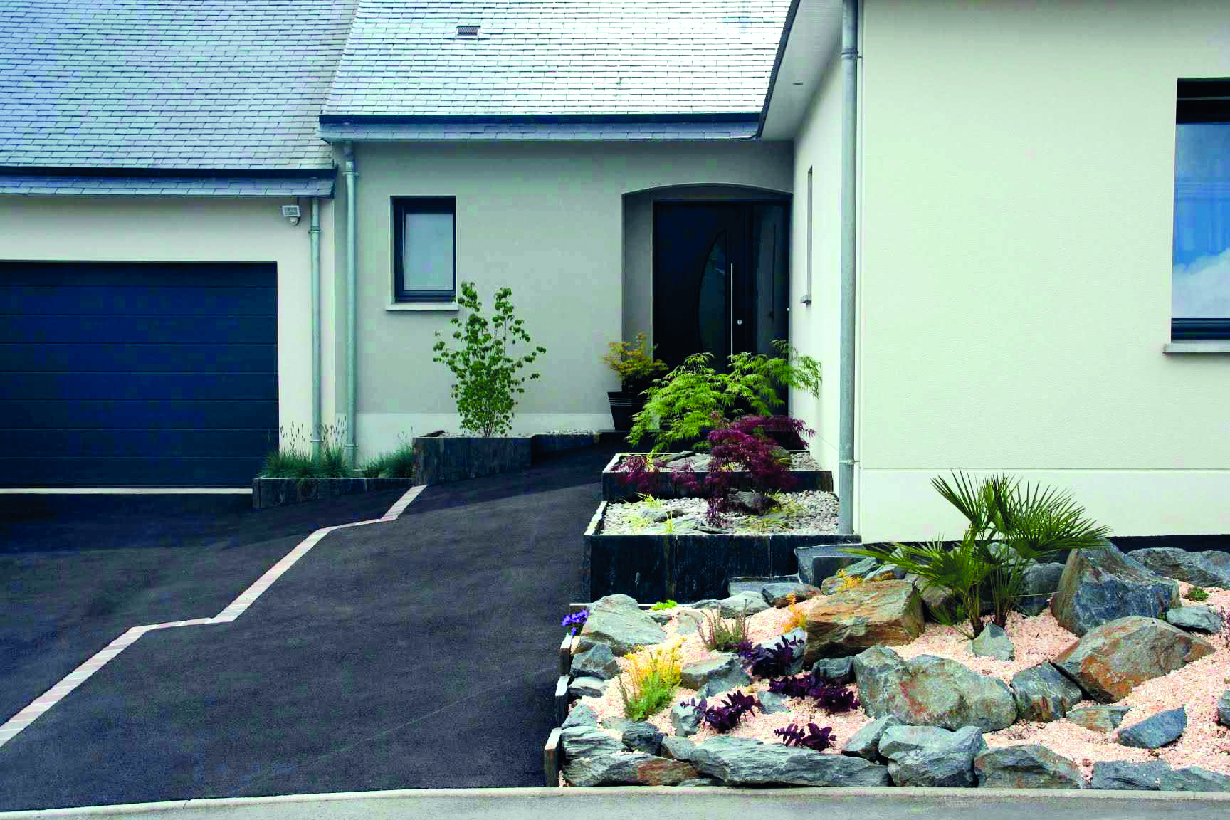 Entrée de maison avec allée en enrobé, massif minéral et plantations