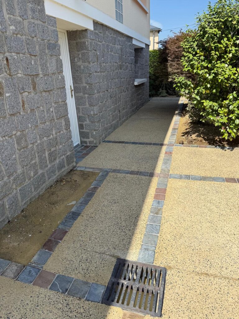 Allée en béton désactivé ocre bordée de pavés le long d'une maison en pierre à Louverné