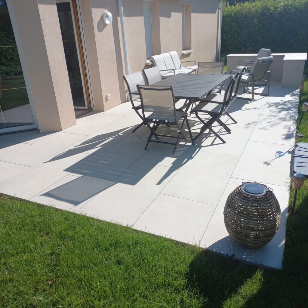 Terrasse en grès cérame beige posée sur plots, avec salon de jardin, à Laval
