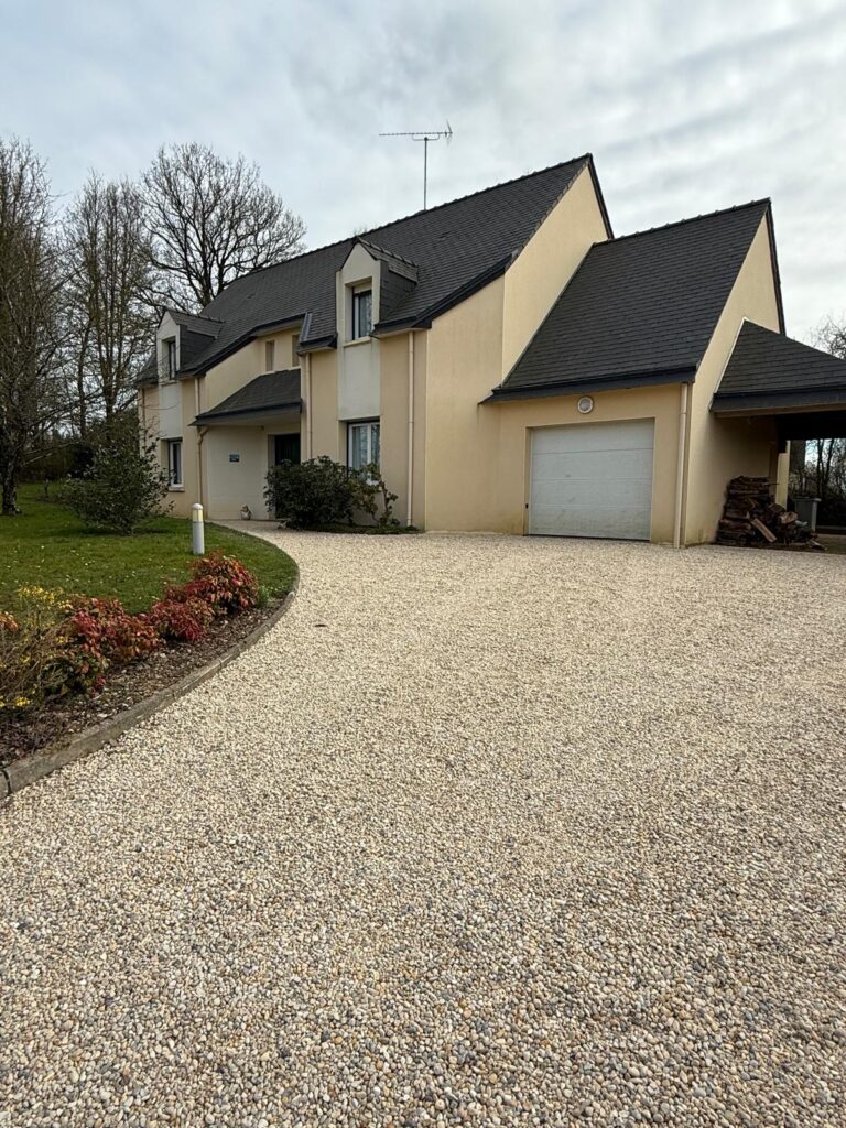Cour carrossable en dalles stabilisatrices remplies de gravier beige devant un pavillon à Saint-Ouen-des-Toits