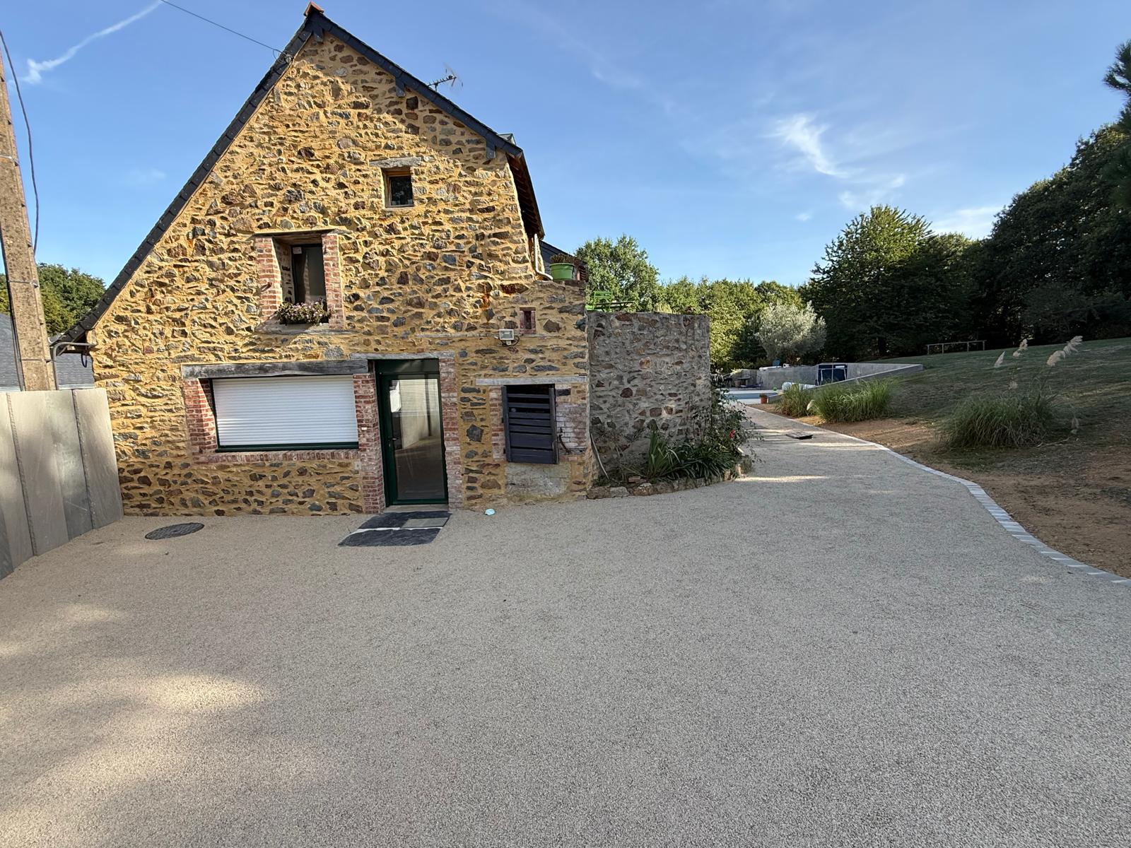 Cour en revêtement gravillonné clair devant une maison en pierre
