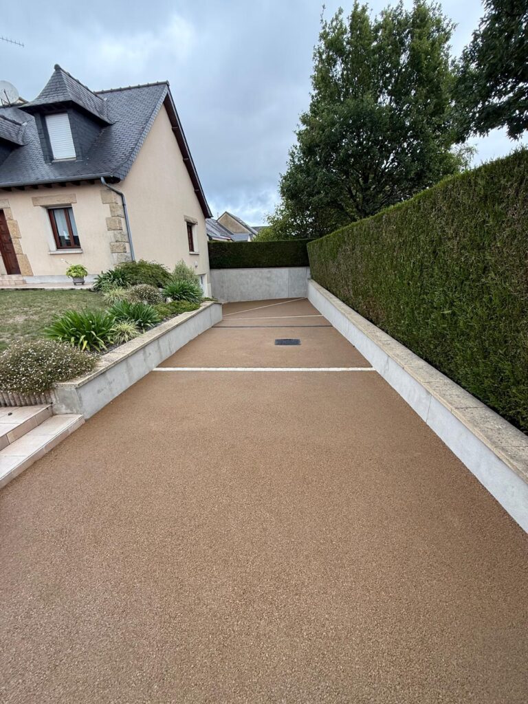 Allée en enrobé beige bordée de chaînettes en pavés menant au garage, à Saint-Berthevin