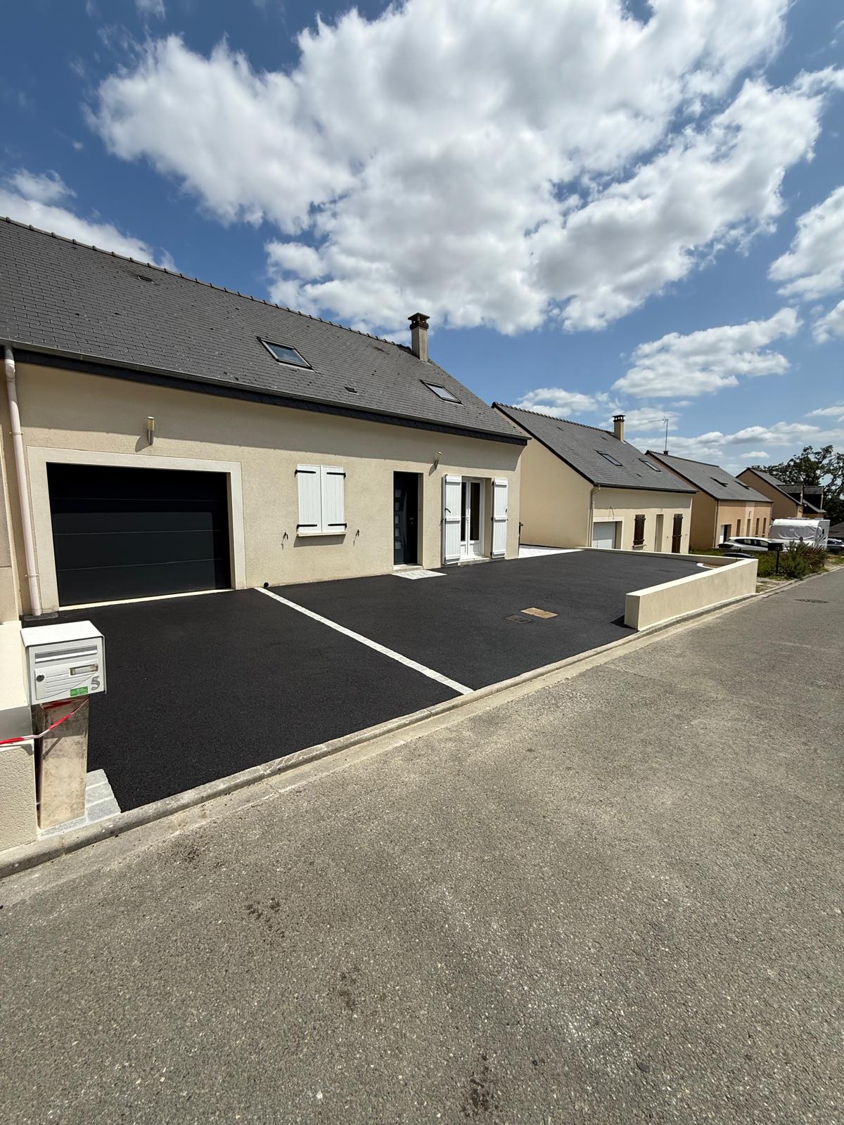 Cour en enrobé noir devant une maison neuve, fermée par un muret enduit