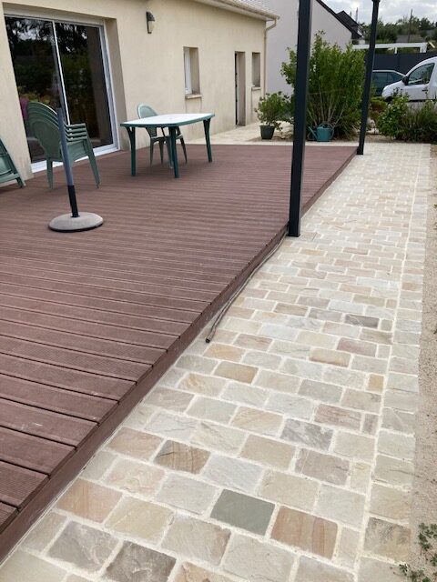 Terrasse en lames composites longée d'une allée en pavés de pierre naturelle