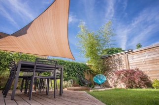 Voile d'ombrage tendue au-dessus d'une terrasse en bois avec salon de jardin