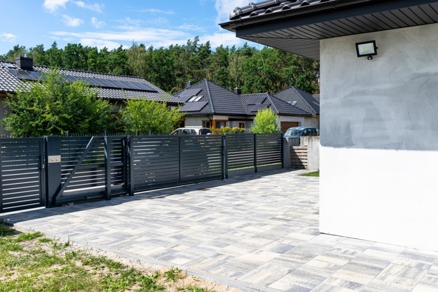 Portail coulissant en aluminium gris ouvrant sur une cour en dalles