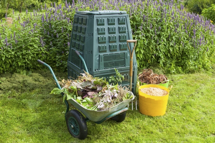 Composteur vert et brouette de déchets verts dans un jardin fleuri