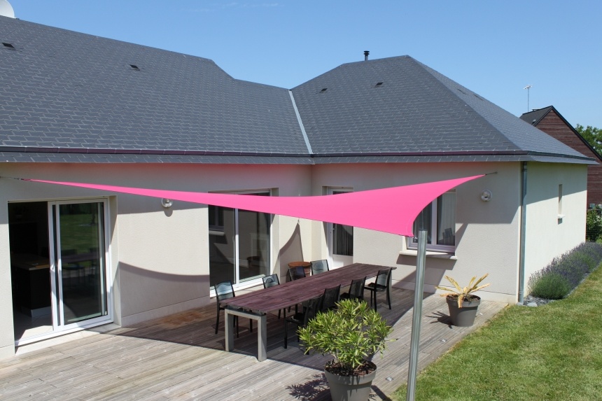 Voile d'ombrage triangulaire rose tendue au-dessus d'une terrasse en bois